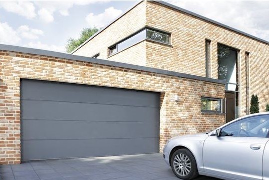 dunkelgraues Garagentor Klinkerhaus mit parkendem Silber Auto 